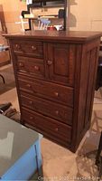 Closed view of wood chest of drawers with multiple drawers and a side cabinet door.