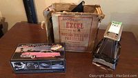 Excel Model 83-U motion picture projector with original cardboard box and pink Cadillac model car box on table alongside the projector.