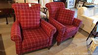 Two matching red plaid upholstered chairs with matching pillows shown side by side in a room setting.