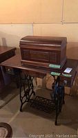 Full view of antique New Williams sewing machine in wooden case on matching wooden table with cast iron base