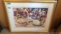 Framed artwork showing potted pansies in cream colored pots with a gold frame.