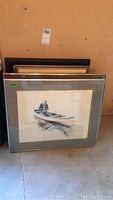 Stack of framed prints with a black and white pencil print of a boy sitting in a canoe in front