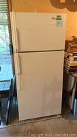 Full view of the white Moffat refrigerator which is a two-door fridge with top freezer, standing in a room next to books and window blinds.