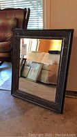 Front angle view of rectangular beveled glass framed mirror with intricate textured dark frame