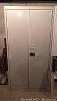 Front view of closed beige metal storage cabinet with double doors and central lock