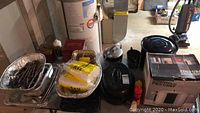 Photo of all kitchen items including pots, pans, silverplate pitcher, ice bucket, and bakeware lined up on floor