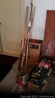 Photo of hockey sticks, pool cues leaning against a wall with boxes and sports gear around.