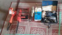 Image showing five tools on a carpet: hedge trimmer, chainsaw, sander, drill, and propane torch, indicating included items and condition.