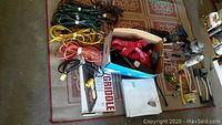 Full view of lot contents showing extension cords, cast iron griddle box, BBQ tool box with straps, and other small items on floor