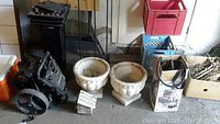 Wood and masonry sprayer, two white decorative bird house planters, golf caddy wheel and bagged item shown on concrete floor in garage area