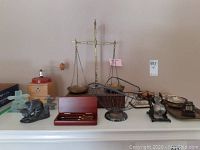 Wide shot showing all items on shelf including balance scale, soapstone carving, Peugeot coffee grinder, inukshuks, wire wine bottle holder, pen set, mini cash register and small bowls