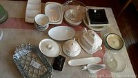 Top down view of various serving ware items including platters, bowls, butter dishes, a gravy boat, a soup tureen, and relish trays arranged on a table.