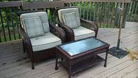 Overview of two wicker armchairs with cushions and rectangular wicker coffee table on deck