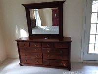Front view of wood dresser with attached mirror showing 11 drawers with metal knobs.