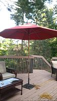 Red fabric patio umbrella fully open on a wooden deck with outdoor seating, showing its height and size.