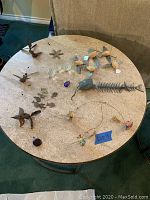 Overview of various mobiles and decorative pieces on round table, including wooden birds, crystal pieces, metal fish skeleton, and wooden parts shaped like birds and fish.