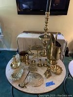 Photo showing entire collection of 17 assorted brass items on round table, including large pitcher and candle holder