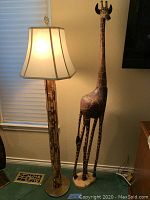 Overall view of carved giraffe statue beside lit floor lamp