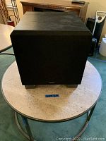 Front view of black cube-shaped Velodyne subwoofer with fabric grille.