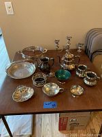 Full collection of 12 silver-plated items including teapot, creamers, candlesticks, and trays laid out on table.