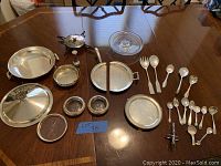 Photo showing entire collection of silver-plated plates, spoons, bowls, shakers, and glass butter dish on wooden table.