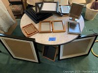 Photo showing a large assortment of frames on and around a round table, 18 in total, of various sizes and materials.