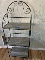 Front view of bakers rack showing three marble shelves and decorative black metal frame.