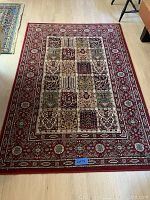 Photo of a red rug with intricate floral and geometric patchwork pattern and a floral medallion border.