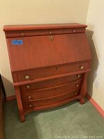 Red wooden desk with drop-front closed, showing three curved front drawers with brass handles and small upper drawers.