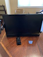 Front view of the Vizio 21-inch TV showing the screen and remote placed in front on wooden surface.
