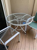 Photo showing round glass patio table with white metal frame and one chair with green fabric seat and backrest.