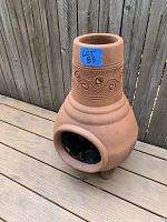 Front-side angle view of terracotta chiminea showing decorative swirl pattern and open fire chamber with three feet at base.