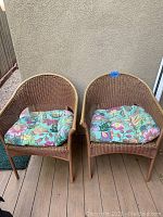 Front view showing two natural-colored wicker chairs with floral cushions on a deck.