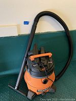 Side angle showing the orange and black Ridgid shop vac with hose and wand.