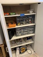 Wide view of the open white cabinet showing assorted hardware organizers, bins, and a black carrying case on shelves
