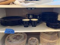 Shelf with stacked black plates, bowls, cups with handles