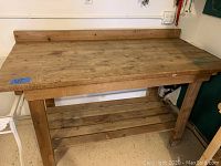 Front view of the wooden work bench showing top surface, back guard rail, legs, and bottom slatted shelf.