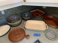 Seven pottery serving pieces arranged on a kitchen counter including bowls, dishes, and trays.