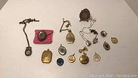 View showing entire assortment of lockets, pendants, and charms arranged on white background including chains and a small framed photo pendant.