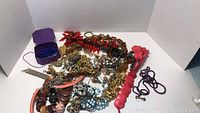 Full lot of various costume necklaces including red, purple, gold-tone, blue, and faux pearl styles along with a small purple box containing a blue beaded item.