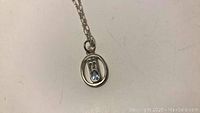 Close-up image of sterling silver XV pendant with blue stone on chain.