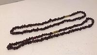 Two red garnet chip necklaces laid out to show length and full strands with gold-tone barrel clasps.