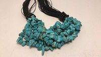 Close-up of chunky turquoise stone beads densely strung together on multiple thin black cords.