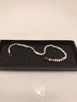 Full view of the petite pearl bracelet inside a black foam-lined box showing the entire string and gold clasp.