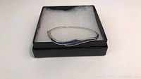 Sterling silver bracelet with blue crystals displayed in a black box with white padding, showing the wave design on the front.