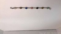 Full length of vintage bracelet showing all seven etched multi-colored gemstones and metal links.