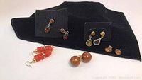 Group of vintage-style earrings arranged on black fabric background including drop and stud pairs in amber, brown, and coral colors.