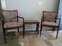 Two chairs and small side table arranged against wall on tiled floor