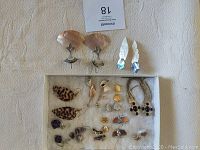 Wide shot of twelve pairs of earrings arranged on cloth showing variety of seashell, artisan silver, and costume jewelry styles.