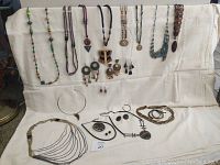Assortment of artisan necklaces, earrings, and pendants laid on white fabric including various material types and designs.